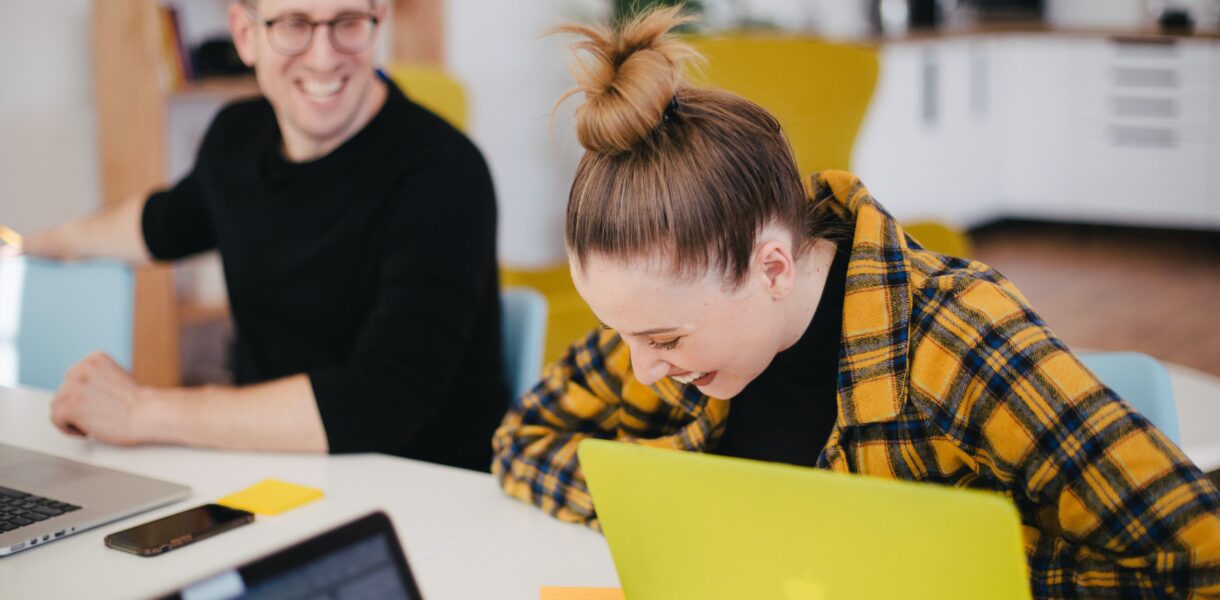 Two happy people sitting in front of their laptops and amusing themselves about something