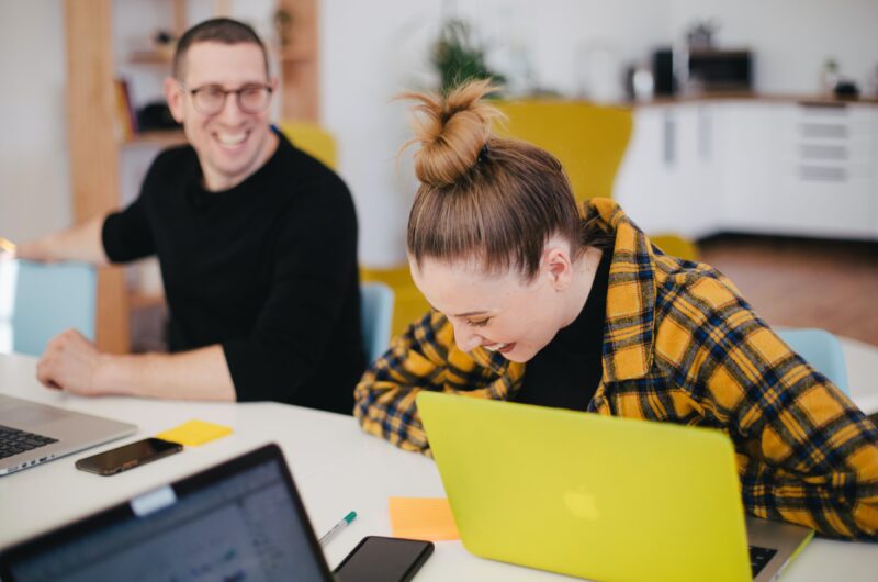 Two happy people sitting in front of their laptops and amusing themselves about something